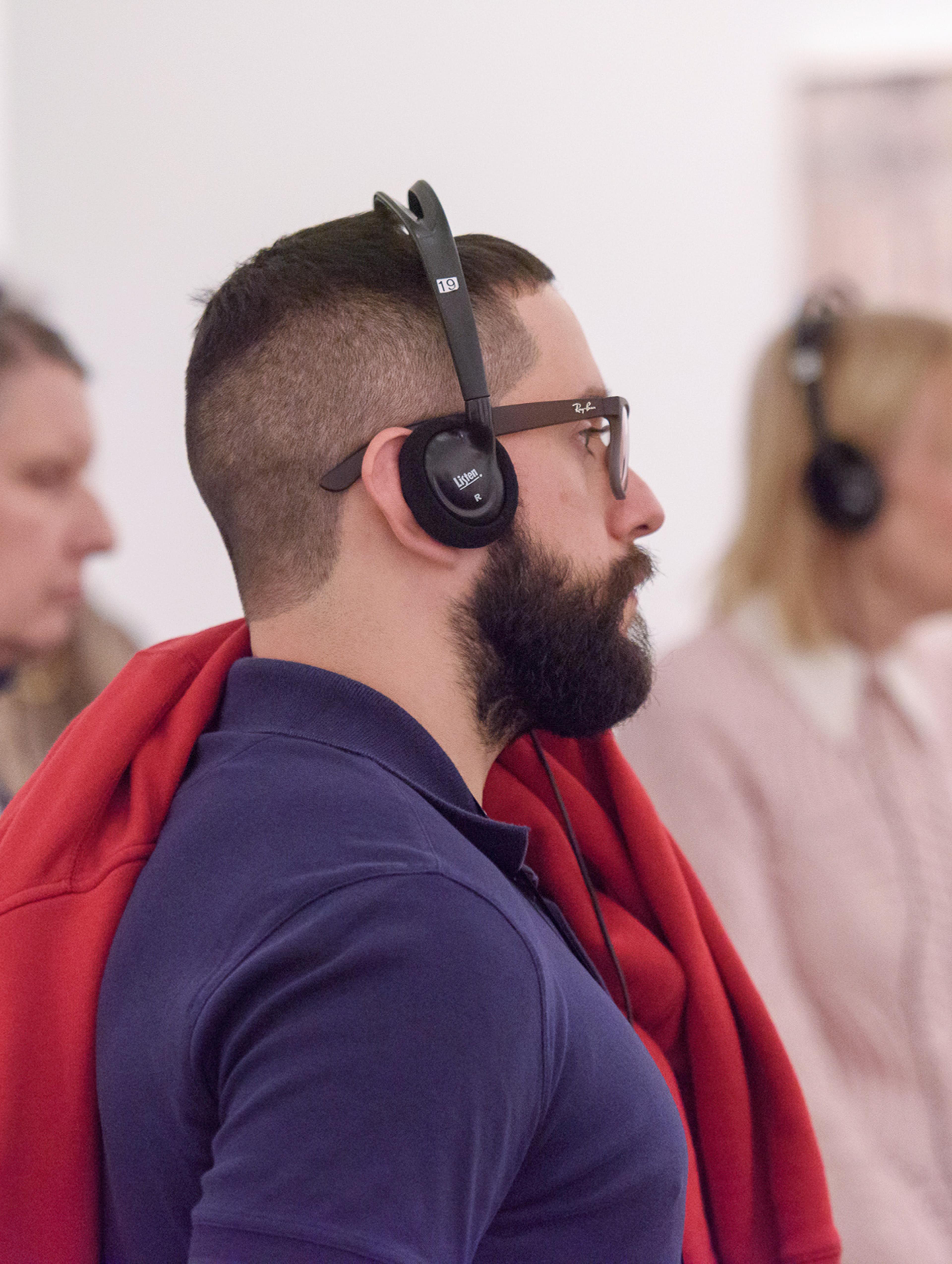 A young man with a beard wears over the ear headphones.