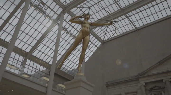 Photograph of a golden statue of a women with a bow and arrow a mid a transparent ceiling with light streaming in