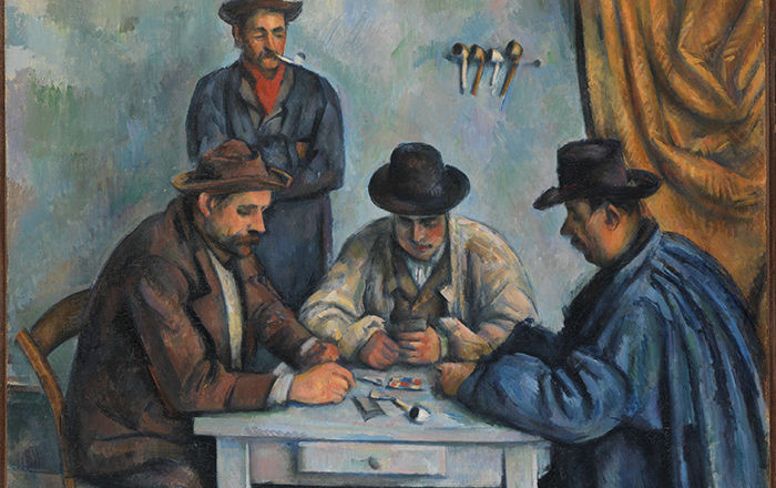 Detail of The Card Players by Cezanne. This oil painting depicts three men with hats seated at a small blue table playing cards while a fourth man stands behind them watching them play. A heavy yellow curtain hangs on the left side of a room with blue walls.