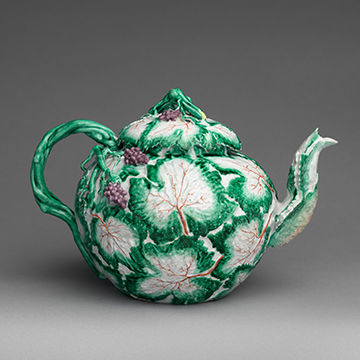 A green and white teapot decorated with trees and blackberries.