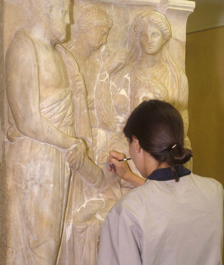 A conservator treating a late Classical Greek funerary stele with a handheld tool