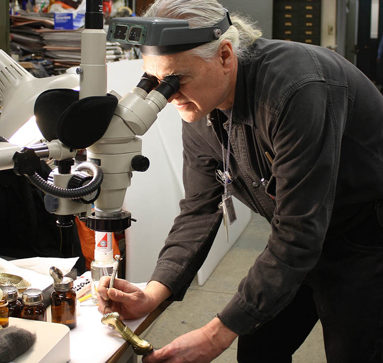 A conservator looking through a magnifying device to clean a dagger handle