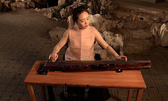 Still image from a video of a woman playing the qin, a plucked zither, in the Astor Chinese Garden Court gallery.