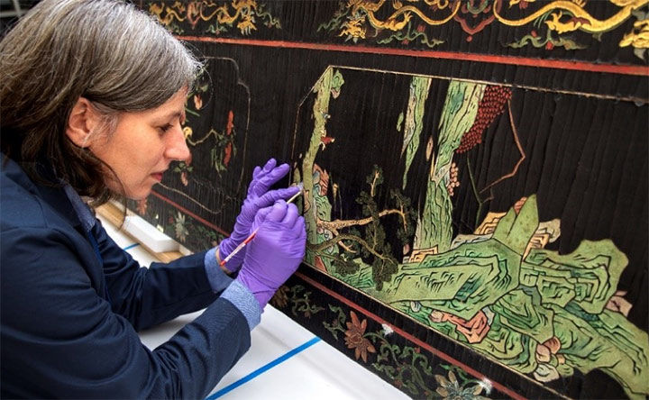 Conservator working on a piece of painted furniture