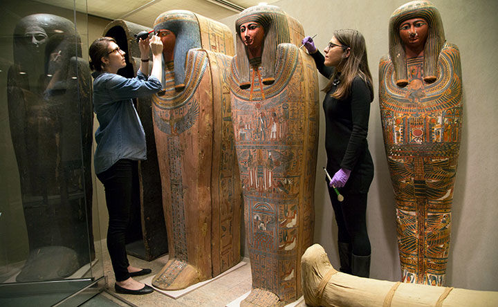 Conservation fellow and conservator use brushes to clean Egyptian coffins