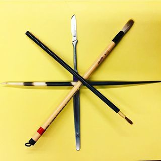 An overhead photograph of three brushes and a scallop knife layered and arranged into a six-pointed star atop a yellow background.