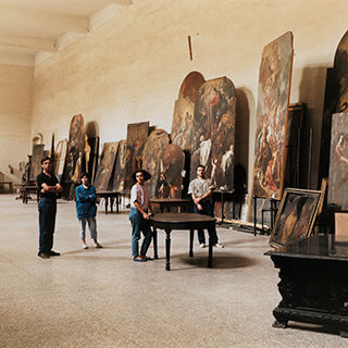 Staff of the Photographs department posing in a large room with many large paintings propped up against the wall