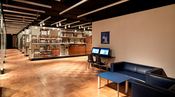 Large room with blue couch, blue coffee table, two computers, and furniture in display cases. 