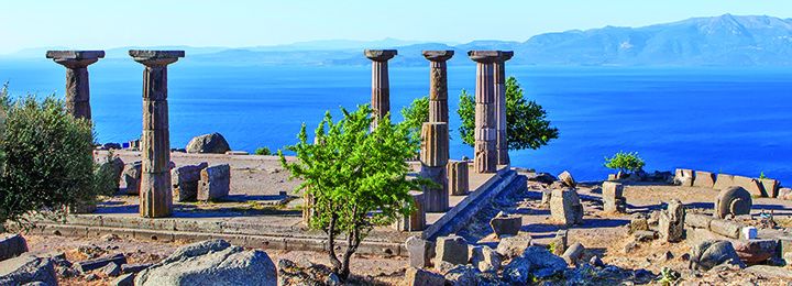 View of ancient ruins and columns in Troy, Turkey in front of ocean and mountains 